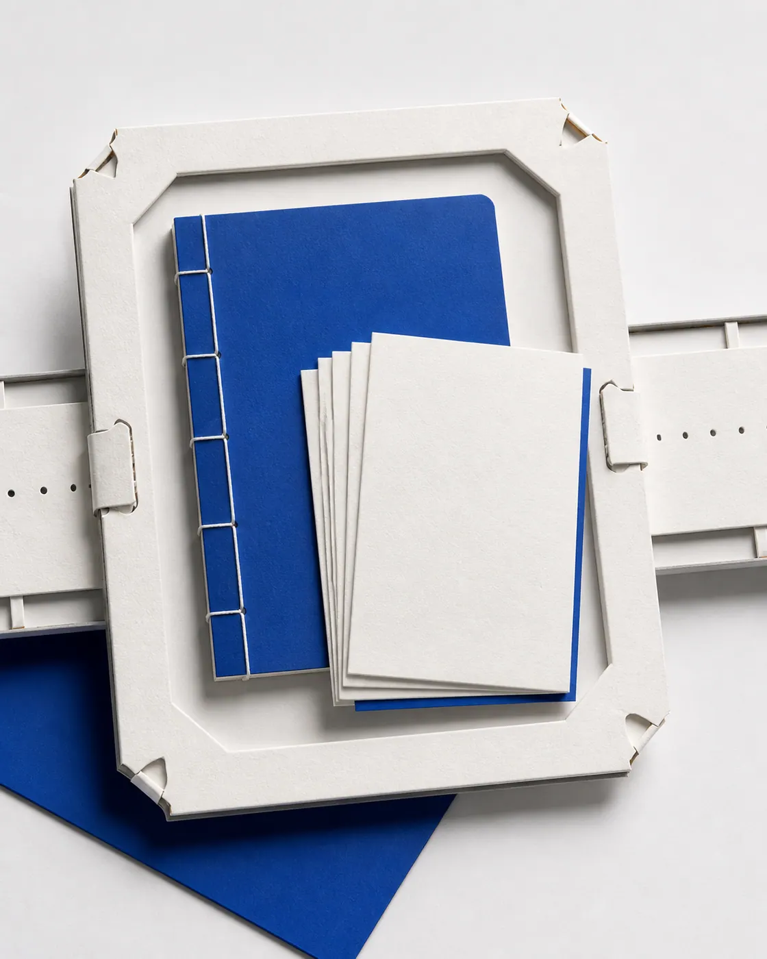 Blank blue thread-bound notebook and postcard stack held in a silver paper carrier